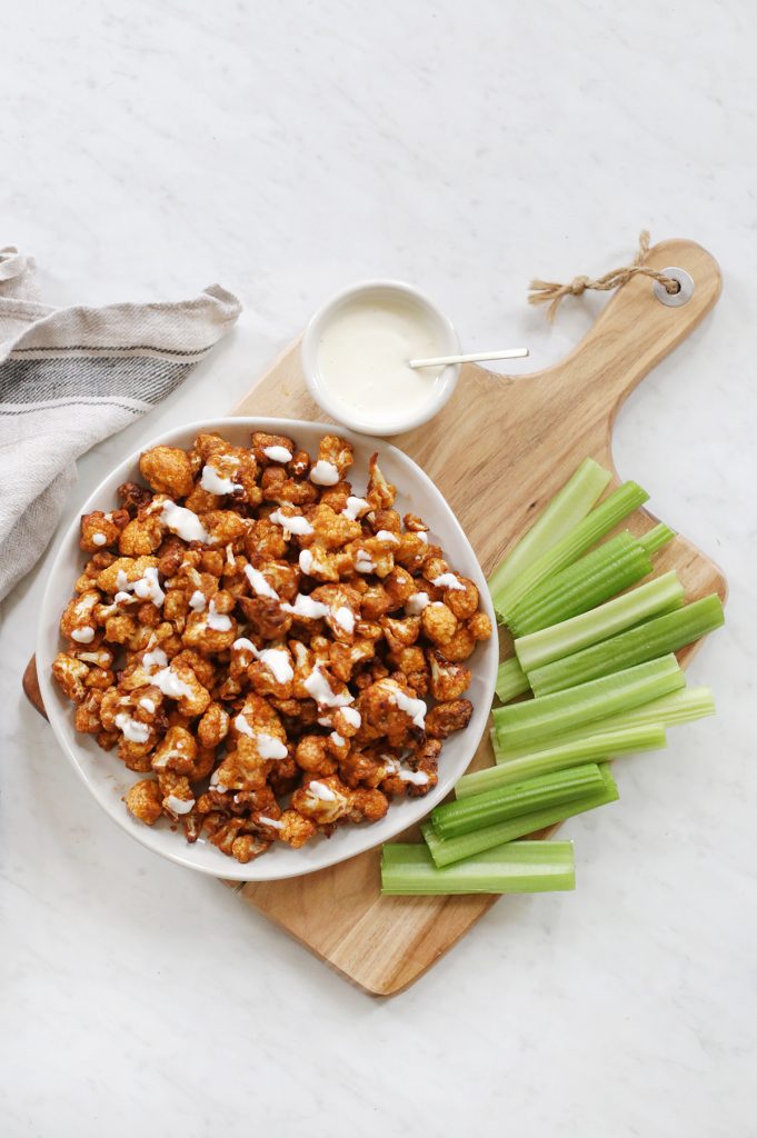 buffalo cauliflower on white plate with celery and blue cheese beside it