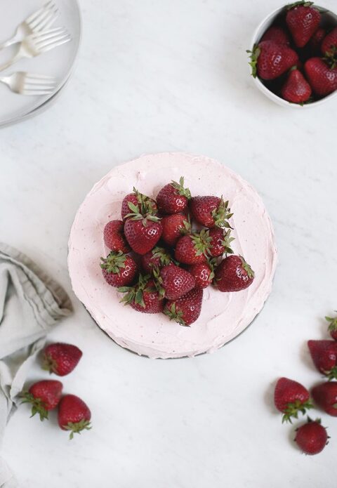 over head view of top of pink frosted cake with pile of strawberries on cake