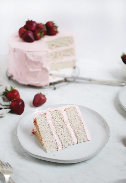 3 layer cake with pink frosting on white plate with large cake behind plate