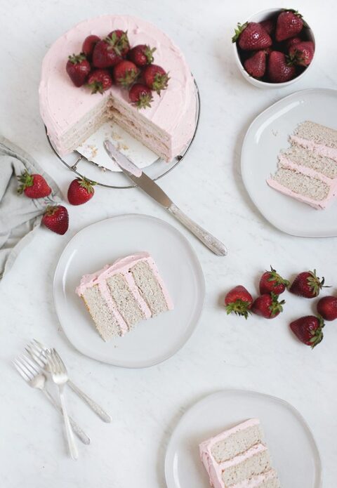 a sliced cake with strawberries on it with plates with cake slices on them surrounding cake