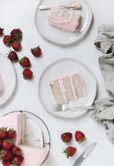 two plates with slices of fresh strawberry cake on them with strawberries surrounding plates