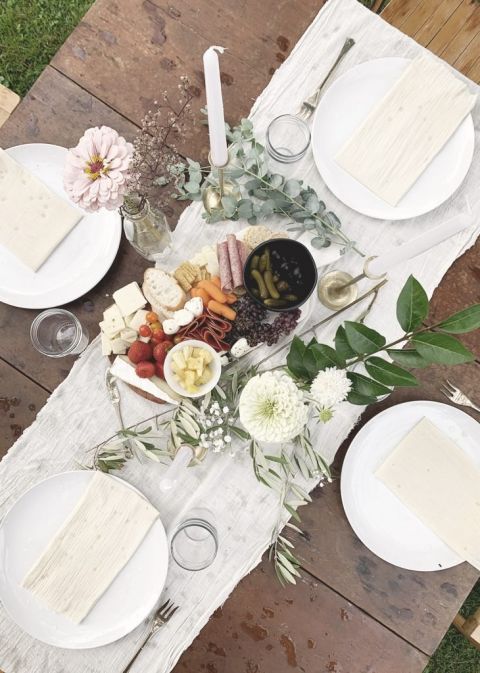 table setting with white runner and green branches with charcuterie board