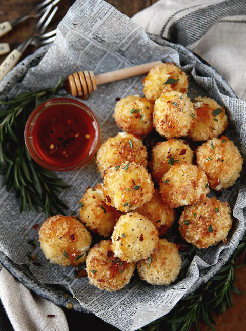metal plate filled with baked goat cheese balls that are drizzled with hot honey and chopped rosemary