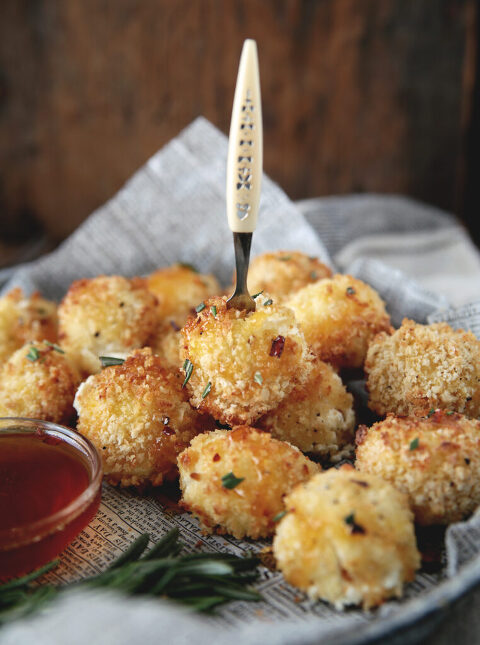 mini appetizer fork sticking into goat cheese ball that is on plate with more goat cheese balls