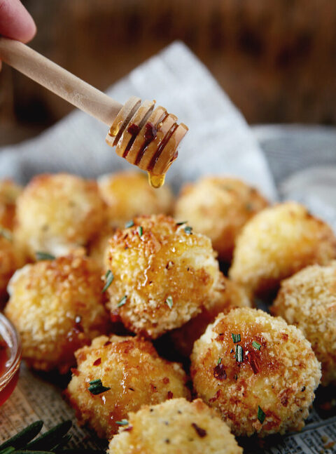 wood honey stick drizzling hot honey over baked goat cheese balls