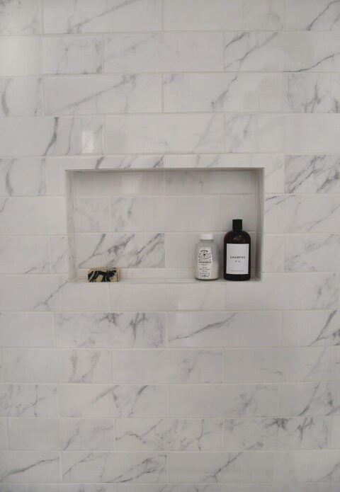 marble tile shower with built in nook holding shampoo bottles