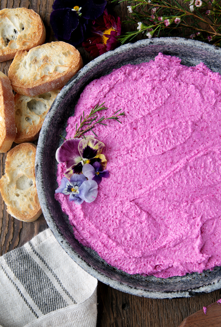 pink roasted beet feta goat cheese dip in metal pie plate with crostini next to plate