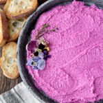 pink roasted beet feta goat cheese dip in metal pie plate with crostini next to plate