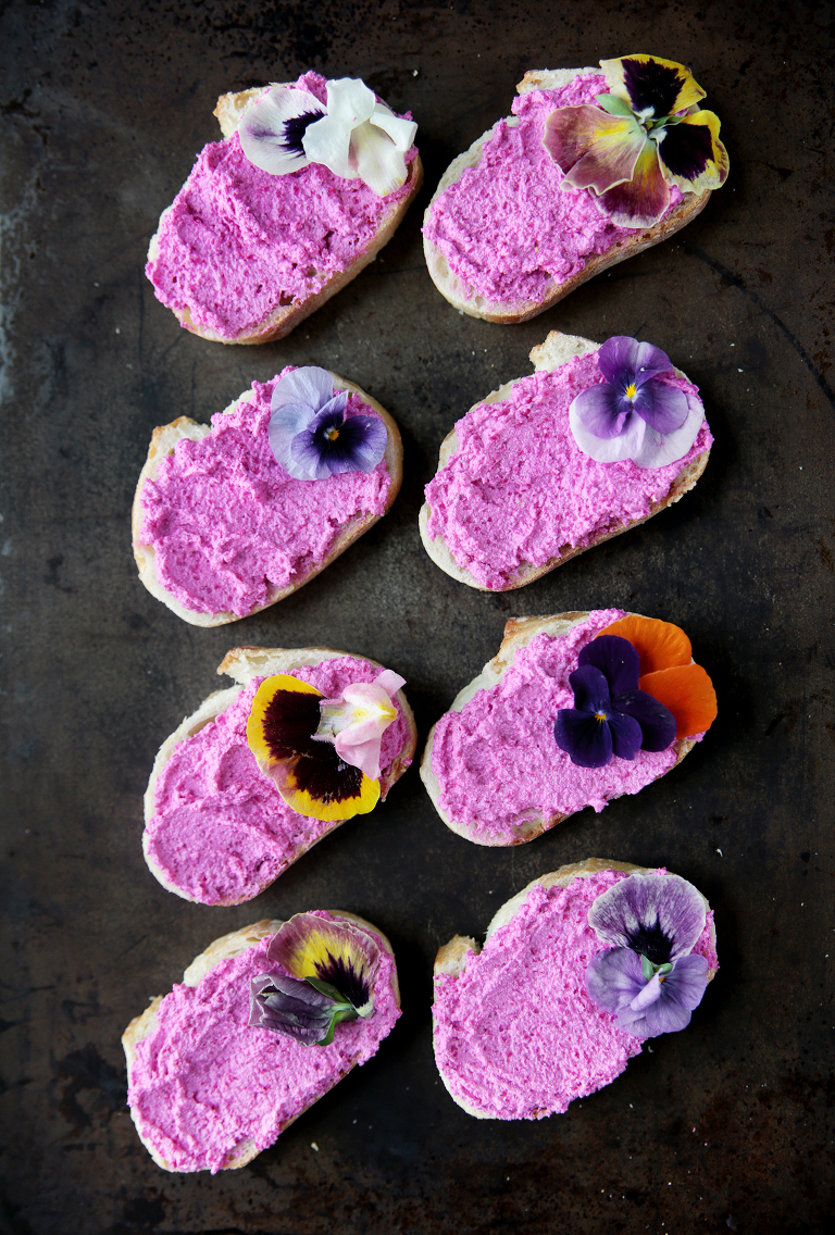 eight crostini topped with pink beet feta goat cheese and edible flowers