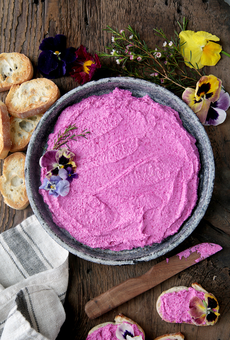 metal pie plate filled with pink beet feta goat cheese dip with crostini toast and edible flowers next to pan