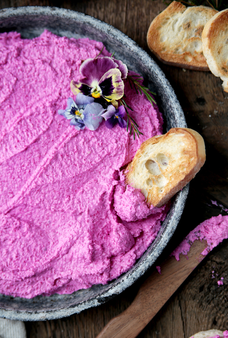 pink beet goat cheese dip in vintage metal pie plate with crostini sitting on edge of plate with wood knife laying next to plate