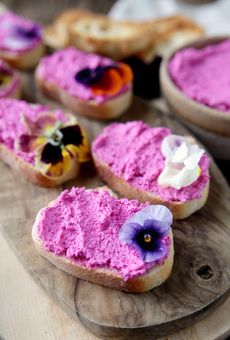 close up of roasted beet whipped feta goat cheese on crostini bread topped with edible flowers