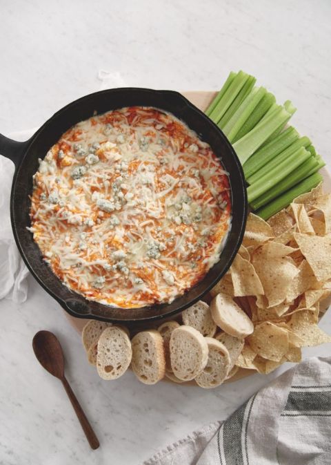 black skillet with buffalo chicken dip in it surrounded by celery, chips and bread