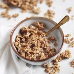 bowl of maple granola with milk and spoon in bowl with granola around bowl