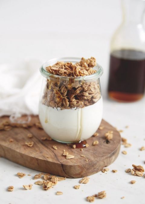 small jar filled with yogurt and granola with maple syrup jar behind it