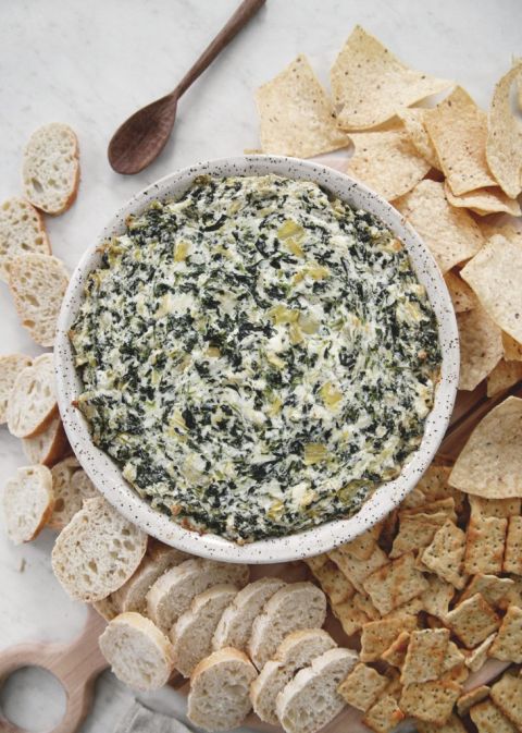 dish with hot artichoke spinach dip in it surrounded by bread, chips and crackers