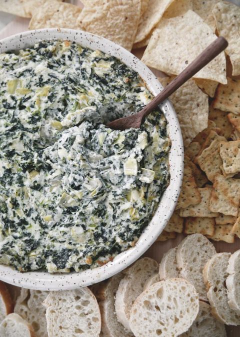 round baking dish with spinach and artichoke dip in it surrounded by chips, crackers and bread