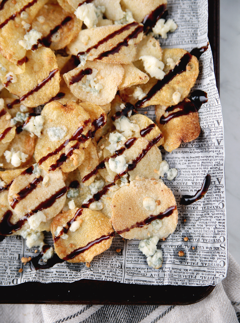 corner of baking tray that has potato chips on it with blue cheese and balsamic glaze on top of chips