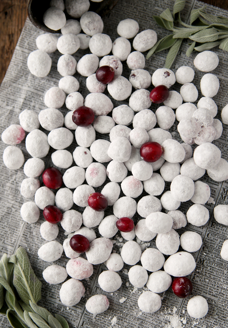 overhead shot of powdered sugar covered cranberries laying on food newsprint with sage on the side