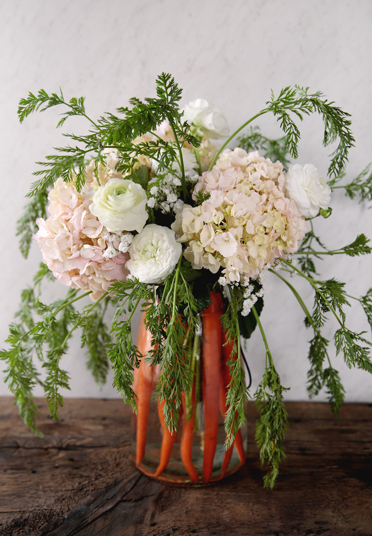 clear vase filled with carrot flower arrangement sitting on wood board