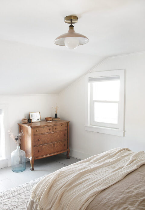 bedroom with antique dresser and a beige and brass ceiling light