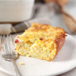 side view of cut piece of cheesy egg casserole on plate with fork next to casserole