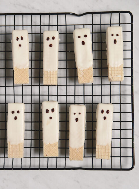 chocolate dipped ghost wafer cookies on black cooling rack