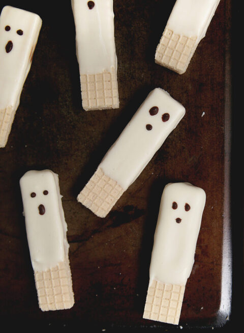 vanilla wafer cookies dipped in white chocolate with chocolate ghost face on dark cookie sheet