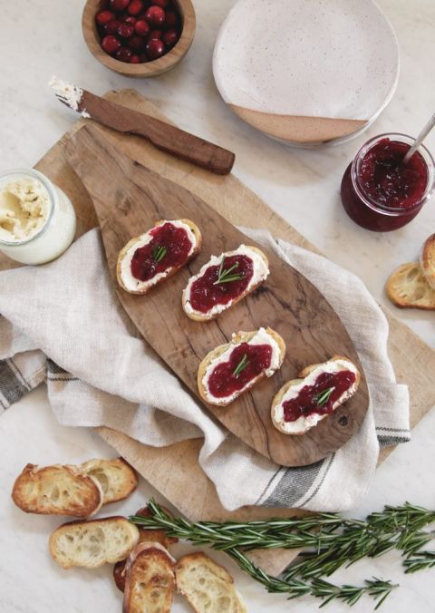 cutting board with cranberry whipped feta crostini on it surround by ingredients