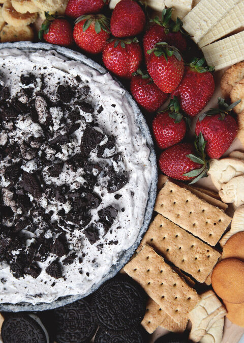 oreo dip in metal pie plate with strawberries, graham crackers, oreos and cookies surrounding pie plate