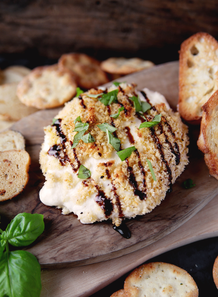 ball of crispy baked burrata cheese on wood cutting board with a balsamic glaze on top and fresh chopped basil on it