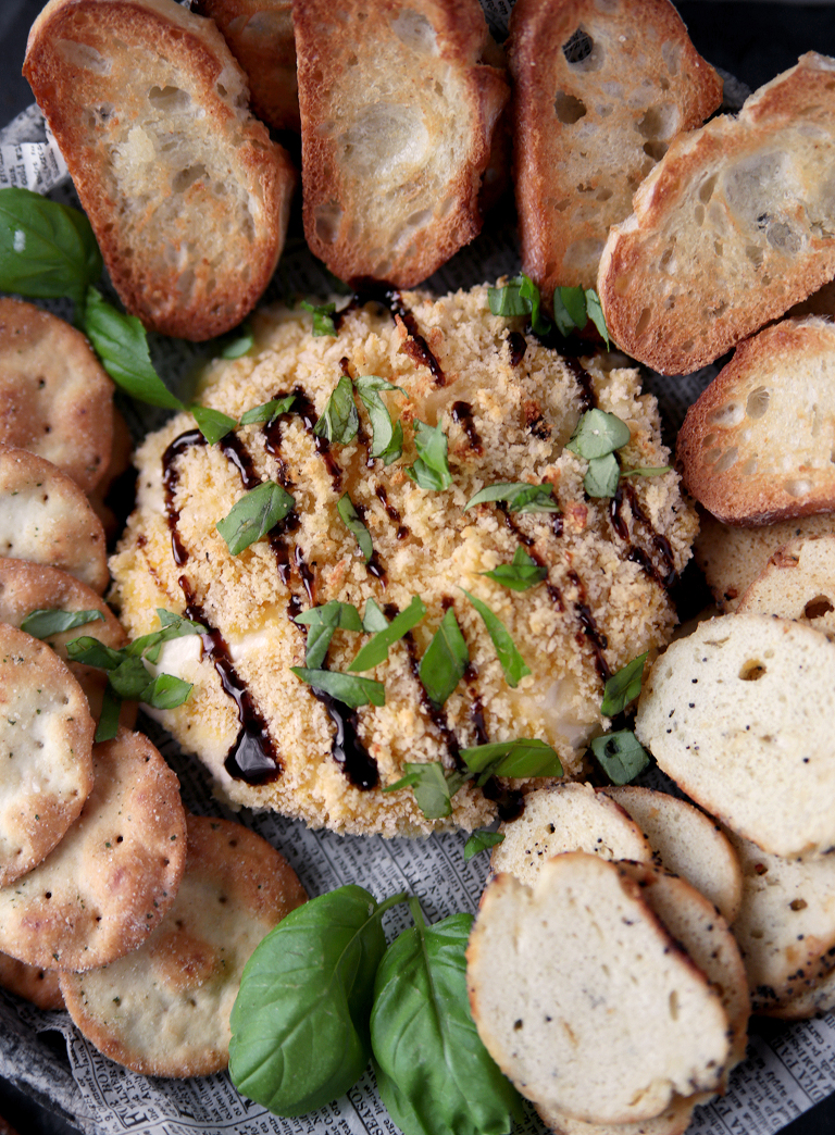 ball of burrata cheese that has panko crumb coating and balsamic glaze on it with chopped basil surrounded by crackers