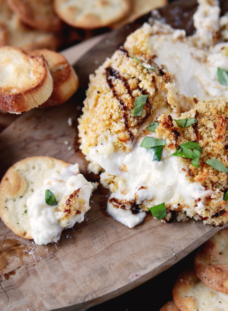 ball of burrata cheese on wood cutting board with balsamic glaze drizzled on top with fresh chopped basil with cracker dipped into cheese