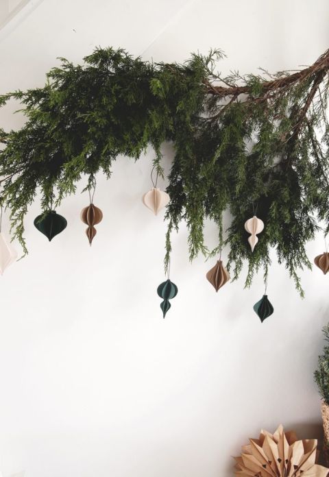 greenery branch on wall with paper ornaments hanging on it