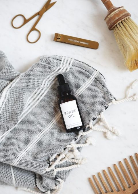 bottle of beard oil lying on towel by scissor, comb and nail clippers