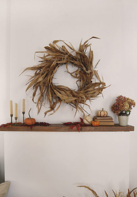 rustic cornhusk wreath above wood mantel with pumpkins and candles on mantel
