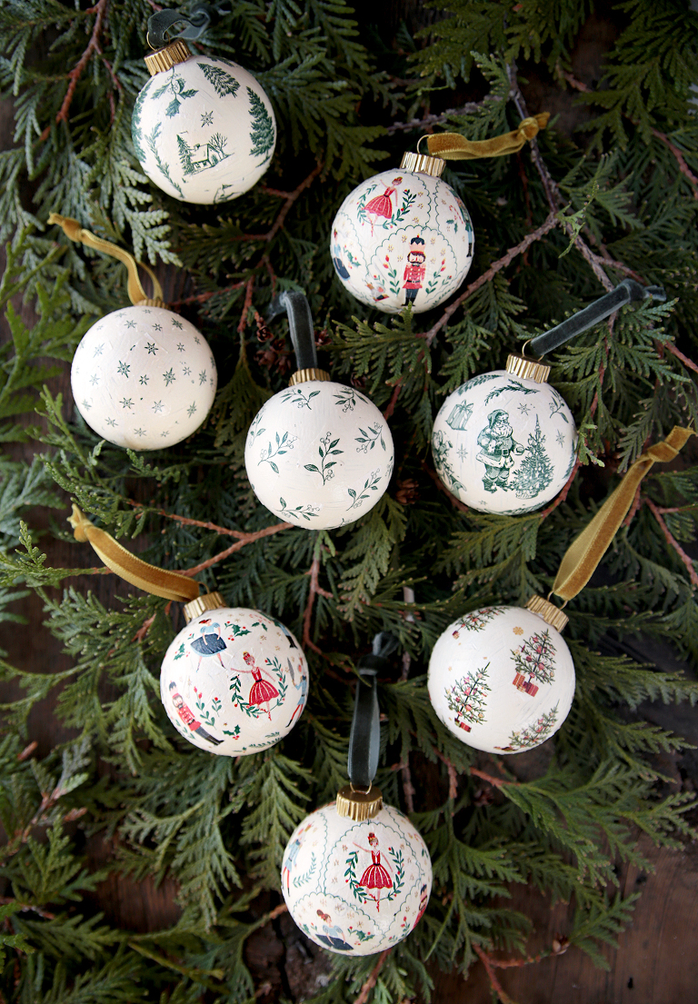 eight decoupage ornaments laying on greenery