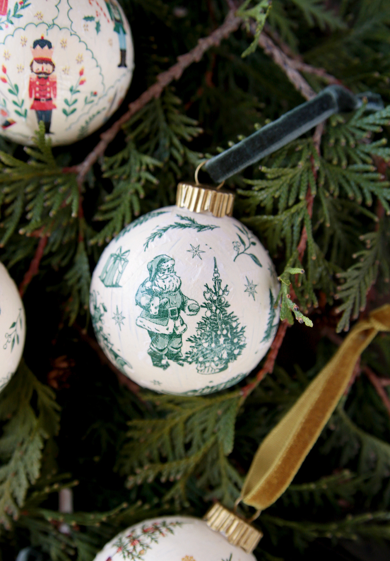 green and white santa decoupage ornament laying on greens