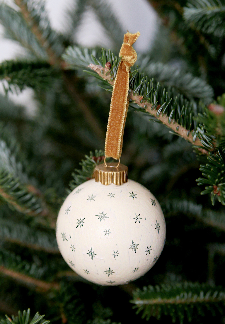 green and white star ornament with gold ribbon hanging from tree branch