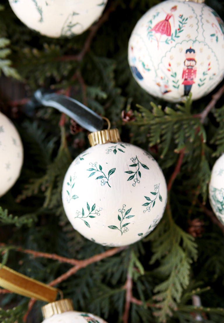 green and white floral decoupage ornament laying on greenery branches