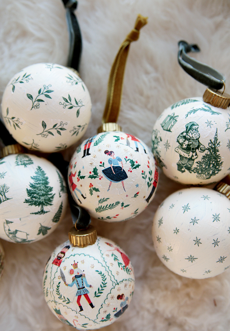6 decoupage ornaments with ribbon laying on white sheepskin rug