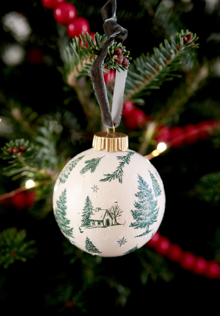 green and white woodsy cabin decoupage ornament hanging on christmas tree branch