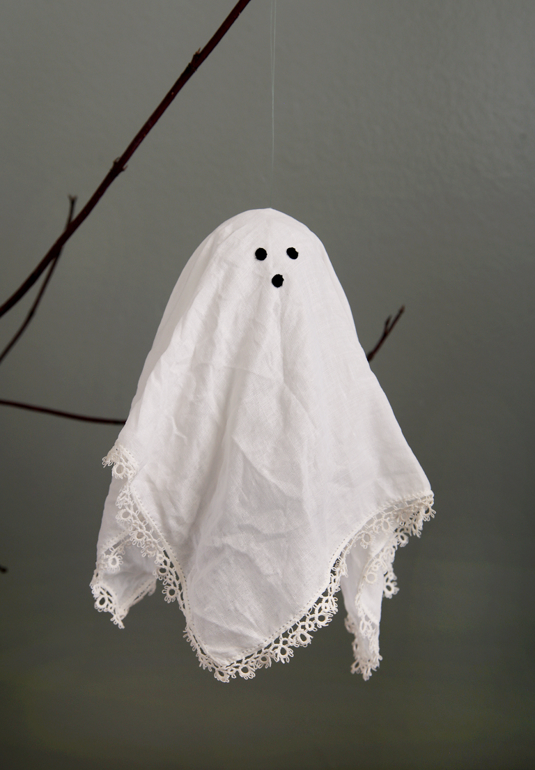diy doily ghost hanging from branch in front of gray wall