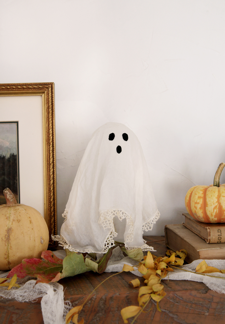 doily ghost on mantel next to pumpkins and dried leaves