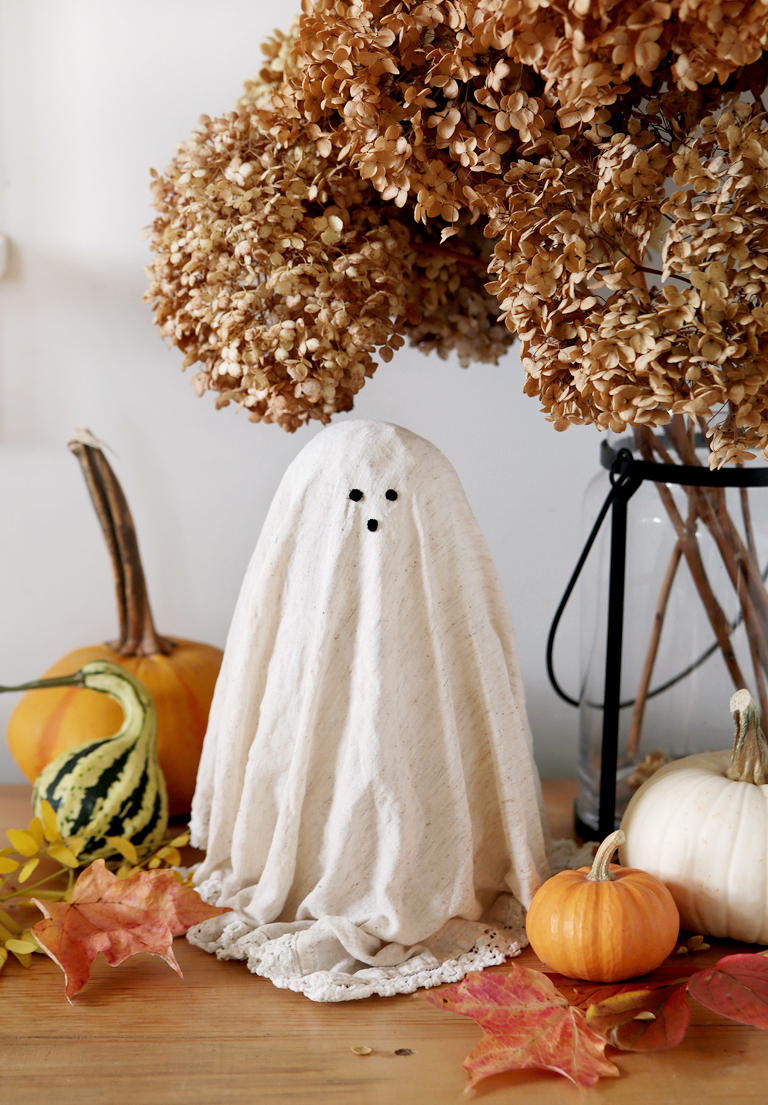 diy doily ghost on wood shelf next to dried hydrangeas and pumpkins