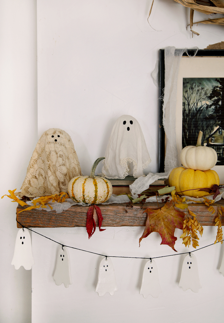 doily ghosts on mantel with pumpkins next to them with clay ghost garland hanging from mantel