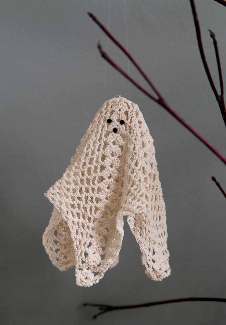 lace doily ghost hanging from branch in front of gray wall