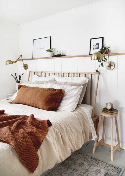 bed against white wall with wood shelf above and brass lamps on wall