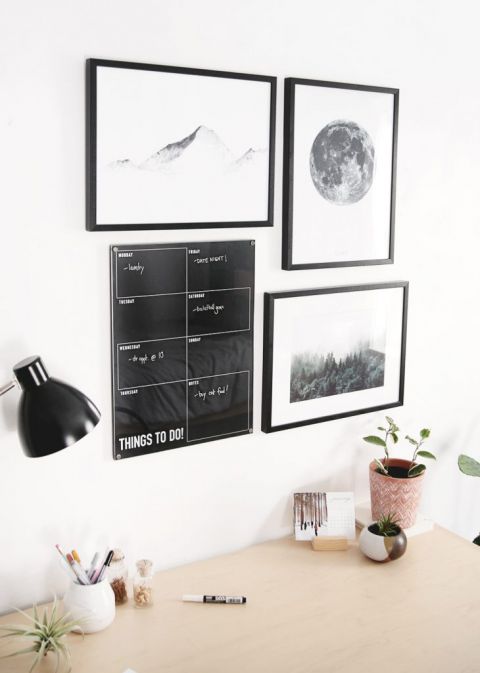 dry erase calendar hanging on wall above desk with art prints around it