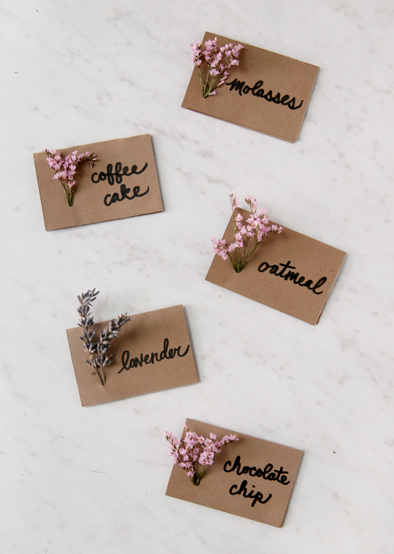 five food labels with fresh flowers in them sitting on marble board